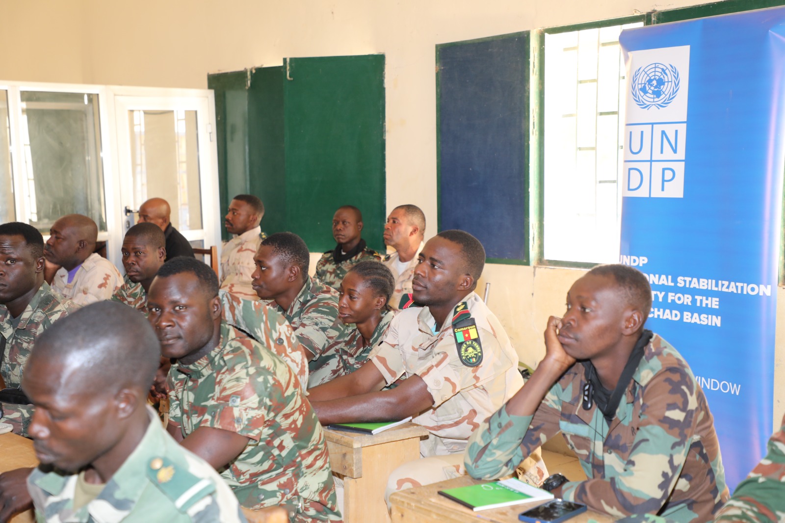 Group of uniformed personnel seated around a table in a room; UNDP banner visible.