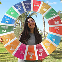 A woman smiles while holding a colorful circular display of sustainability goals outdoors.