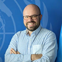 Man with a striped blue shirt and folded arms, blue background.