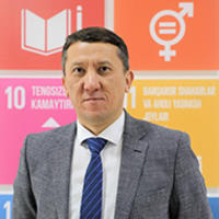 Photograph of a man in a gray suit and blue striped tie, standing before pink and orange SDGs banners.