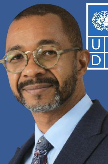 Portrait of a man in a suit and glasses, with a UNDP logo on a blue background.