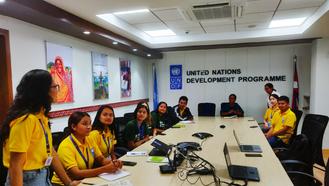 A group of people in yellow shirts sits around a conference table at a UN office.
