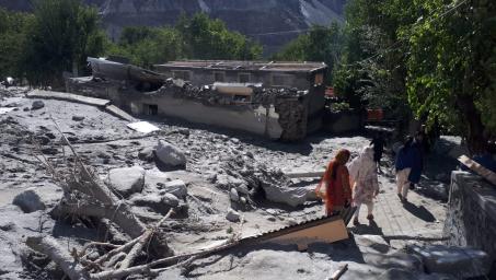 A group of people walk through a destroyed house.