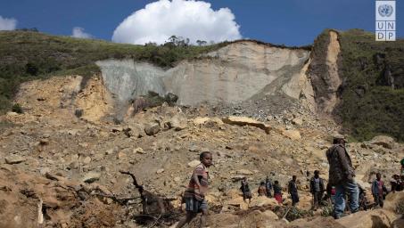 Wide shot of collapsed hillside with people walking over rubble