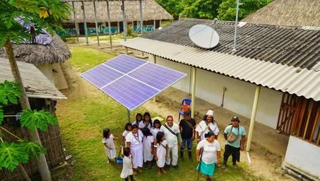 A group of people stands under a solar panel structure in a rural setting.