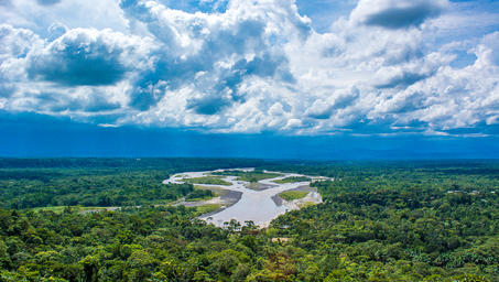 Lush green landscape with a winding river and dramatic clouds above.