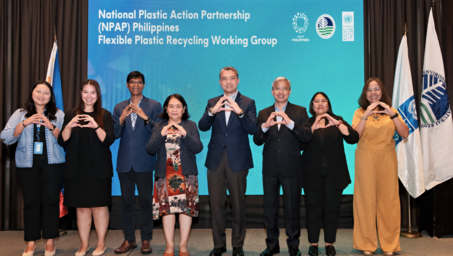 Eight individuals stand together, forming a heart shape with their hands in front of a conference backdrop.