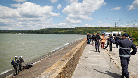 A group of people on a concrete pier by the water, with cloudy skies in the background.