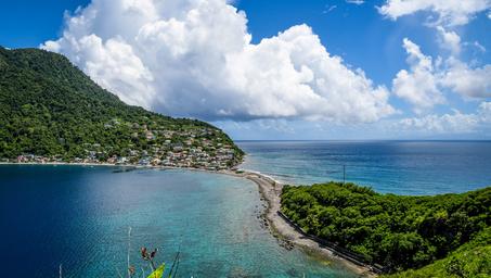 Turquoise waters meet green hills under a bright blue sky with fluffy clouds.