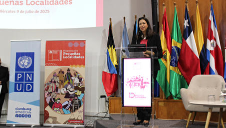 A woman speaking at a podium with flags in the background and banners on display.