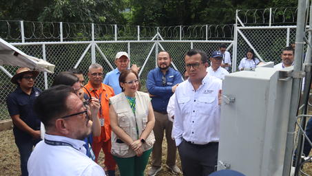 A group of people in work attire gathered around a technical device outdoors, discussing.