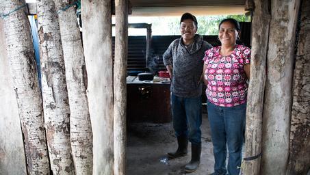 A man and woman smile together in an open doorway framed by wooden posts.