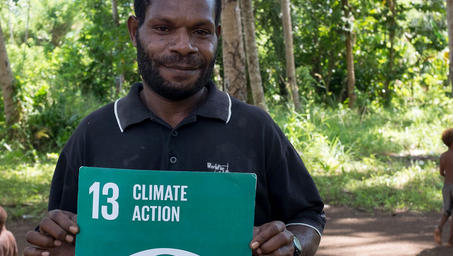 Man holding a Climate Action sign with a globe icon in a sunlit forest.