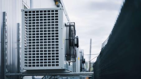 Rooftop HVAC unit with metal grille, pipes, and blue sky in the background.