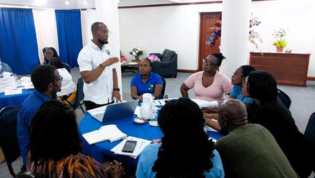 Group of people around a blue circular table; a man in a white shirt speaks to others.