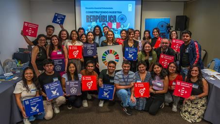 Group photo of a diverse crowd in a conference room, holding red, blue, and white signs.