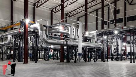 Inside a large industrial plant, a maze of silver pipes and steel supports.