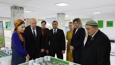 Dignitaries in suits study a scale city-model on a table in a bright room.