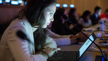 Woman with long hair using a laptop at a conference table.