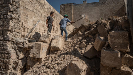 Photograph of two people navigating rubble inside a ruined stone structure.