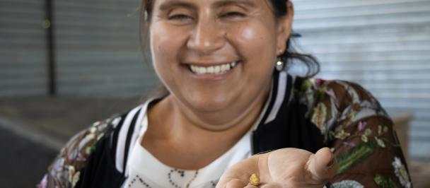 Mujer sonriendo, sosteniendo pepita de oro