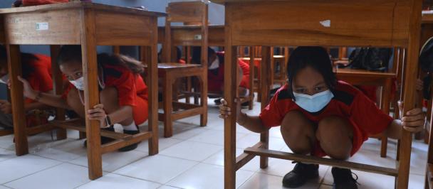 Students in Bali simulate a tsunami by hidding under a school table