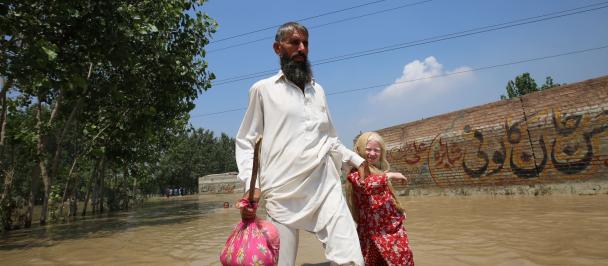 A man holds a girl's hand and as they walk through flood waters.