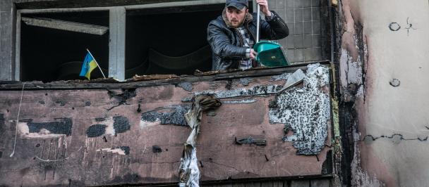 A man clears rubble from the balcony of an apartment damaged by shelling.