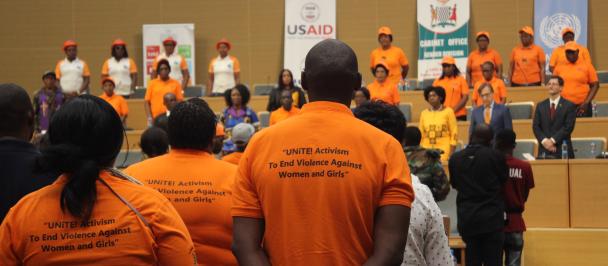 A man wearing a orange t-shirt that reads "UNiTE: Activism to End Violence Against Women and Girls"