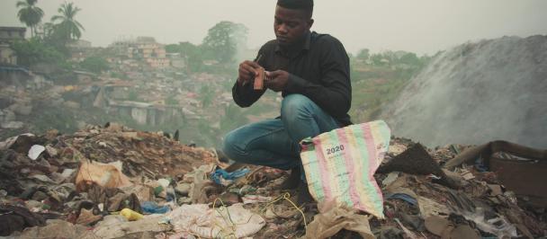 Surrounded by garbage, Alie Mansaray examine a small electronic component.