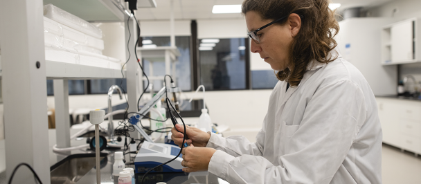 Mujer científica, sentada de túnica, en laboratorio, concentrada trabajando