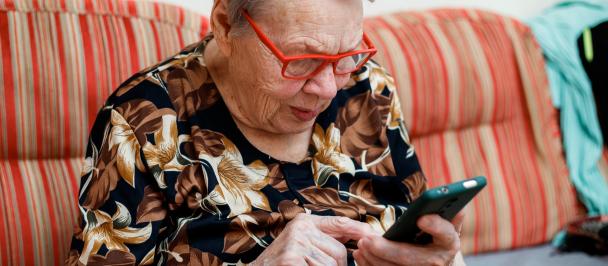 A grey-haired women presumably over 80 is looking at and pointing with her finger at a mobile phone