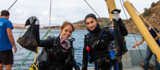Two young woman in scuba gear smiling, looking at the camera holding underwater nets with starfish inside