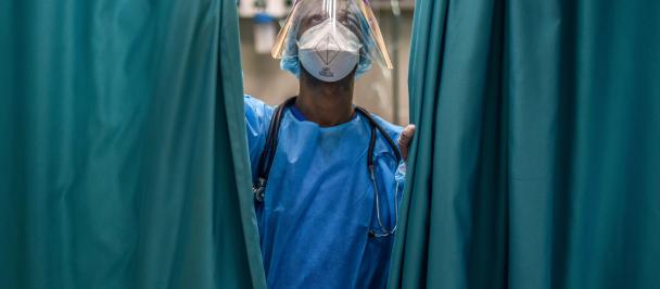 Person in a surgical mask and scrubs stands next to curtains