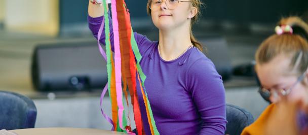A young woman with Down syndrome works with colourful paper ribbons in an art class.