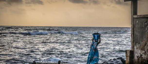 Woman in traditional dress stands by seaside.