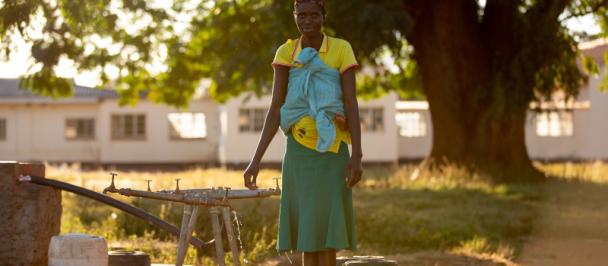 Woman stands at solar powered pump with water containers