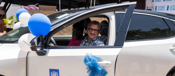 A child smiles while sitting in a decorated white car, balloons nearby.