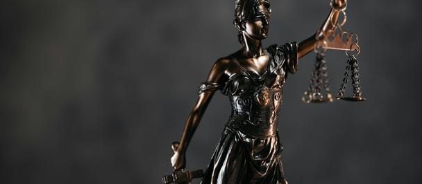 Bronze statue of Lady Justice holding scales and a sword against a dark background.