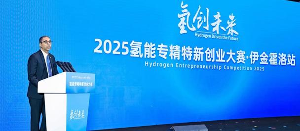 A speaker at a podium presents at a Hydrogen Entrepreneurship Competition with a blue backdrop.