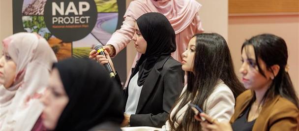 A group of women sitting in a conference setting, focused on a speaker in the background.