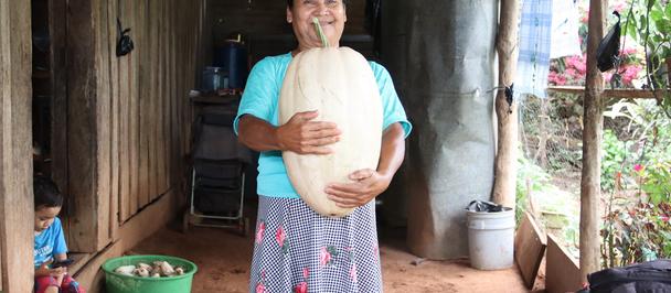 Photograph of a pregnant woman outdoors, teal top and floral skirt, hands on belly.