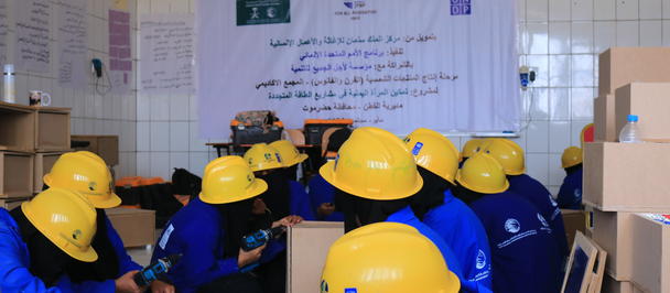 Group of individuals in blue work uniforms and yellow helmets collaborating in a training room.