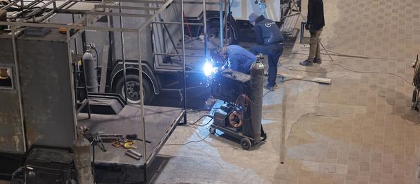 Backstage scene with metal truss, lighting rig, and a technician adjusting gear.