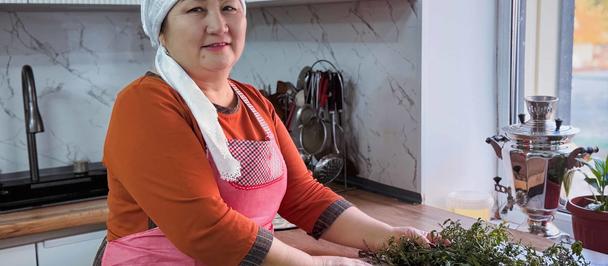 Person wearing orange sweater and pink apron stands at kitchen counter with fresh herbs.