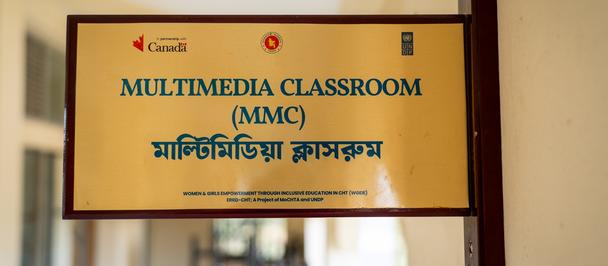 Yellow sign: Multimedia Classroom (MMC) with Bengali text, mounted on a wall in a hallway.