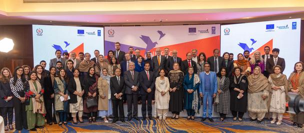 Photograph of a large group of people on stage at a conference, banners in the background.