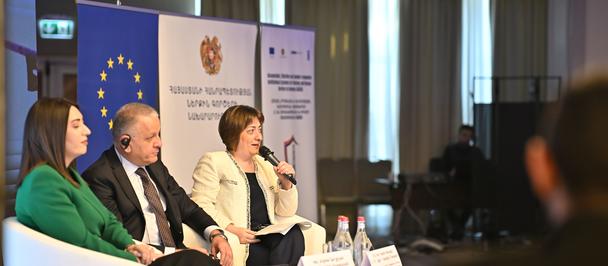 Panel of four speakers on stage at a conference, with EU banners in the background.