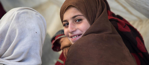 Two women wearing hijabs seen from behind, one brown and one light blue, under a tent.