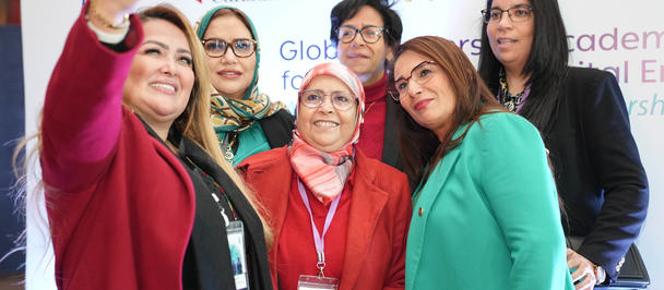 Group of people posing for a photo at an event, banners visible in the background.